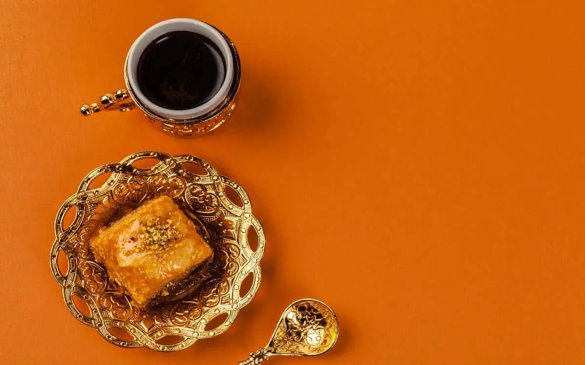 A top-down photo of tukish coffee sat next to a turkish delight on a gold, ornately-decorated tray similar to baclawa